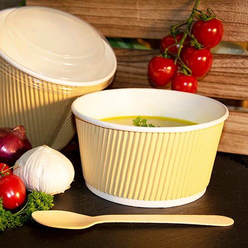 Ein braun-weißer PAPSTAR Ripple Wall Suppenbecher (720 ml) der PAPSTAR GmbH steht mit Suppe gefüllt auf einem dunklen Untergrund neben einem Holzlöffel, Knoblauch, Petersilie, roten Zwiebeln und Strauchtomaten. Im Hintergrund ist ein weiterer Behälter mit Deckel zu sehen.