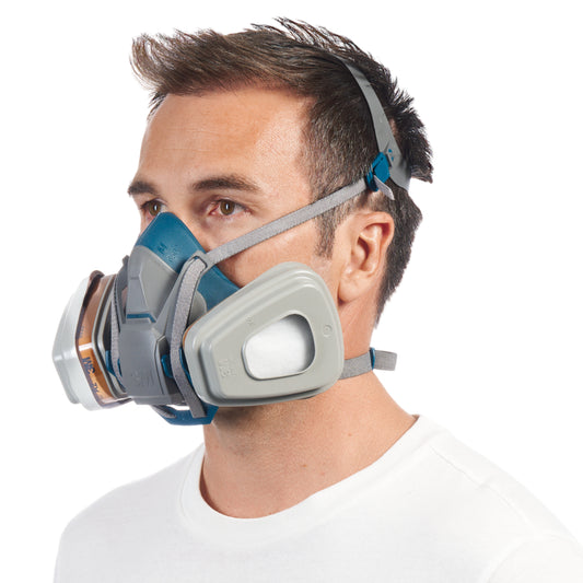 Ein Mann in einem schlichten weißen T-Shirt trägt die 3M™ Quick Latch-Atemschutzmaske 6502QLKIT-1 mit austauschbaren A2P3-Filtern der 3M Deutschland GmbH mit verstellbaren Gurten über dem Kopf und blickt leicht nach links vor einem weißen Hintergrund.
