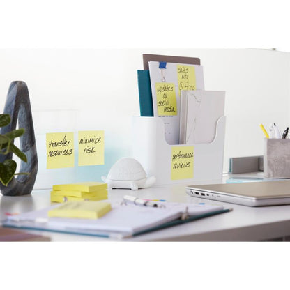 A tidy office desk with Post-it® Super Sticky Notes (76x127 mm, 90 sheets, 100% PEFC) from 3M Deutschland GmbH on a glass divider, along with folders in a holder, a turtle figure, office supplies, a closed laptop, and an open notebook with a pen.