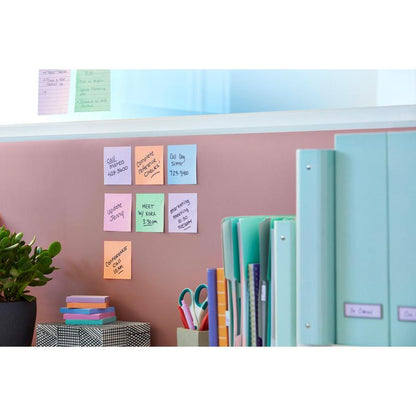 A pink wall with Post-it® Super Sticky Notes (47.6 x 47.6 mm, 90 sheets, 100% PEFC) from 3M Deutschland GmbH, a green plant, a patterned box, scissors, organized folders on the desk, and more notes on a glass plate above.