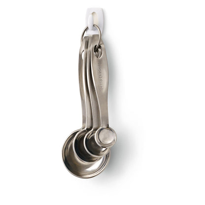 Vier Messlöffel aus Edelstahl an einem Metallring hängen an einem 3M Deutschland GmbH Command™ Mini-Haken, 17006 - sicher befestigt ohne Bohren und leicht und rückstandsfrei von der weißen Wand zu entfernen.