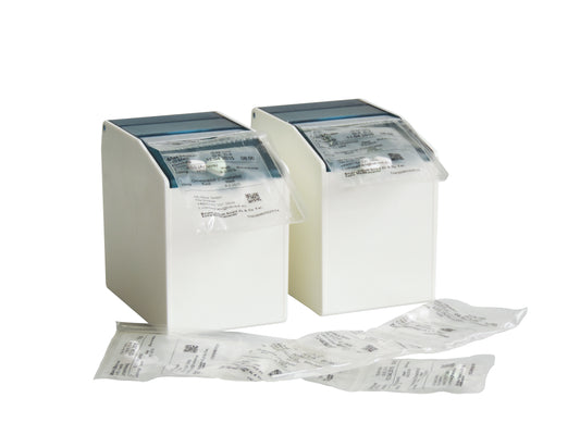 Zwei weiße Novocal Blisterbox-Spender (1 flexible Frontklappe, 2 rückseitige Magnetstreifen, 80 mm, 1 Packung) nehmen versiegelte Medikamentenpackungen auf, mit zusätzlichen Packungen kleiner Produkte auf weißer Fläche vor einfarbigem Hintergrund.