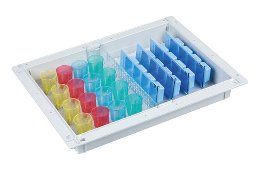 Das weiße Novocal Blistermodul (ABS, 300 x 400 x 50 mm) für 32 Bewohner fasst farbcodierte Zylinder - gelb, rot, blau - und verfügt über vertikale blaue Trennwände auf der rechten Seite für ein platzsparendes Medikamentenaufbewahrungssystem.