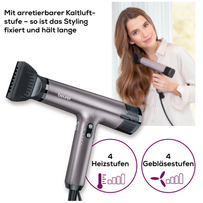 A woman dries her long, wavy hair with the silver Beurer HC 100 High Speed Hair Dryer Excellence from Beurer GmbH with ion function, 4 heat/air settings, and a lockable cold air function in German language.