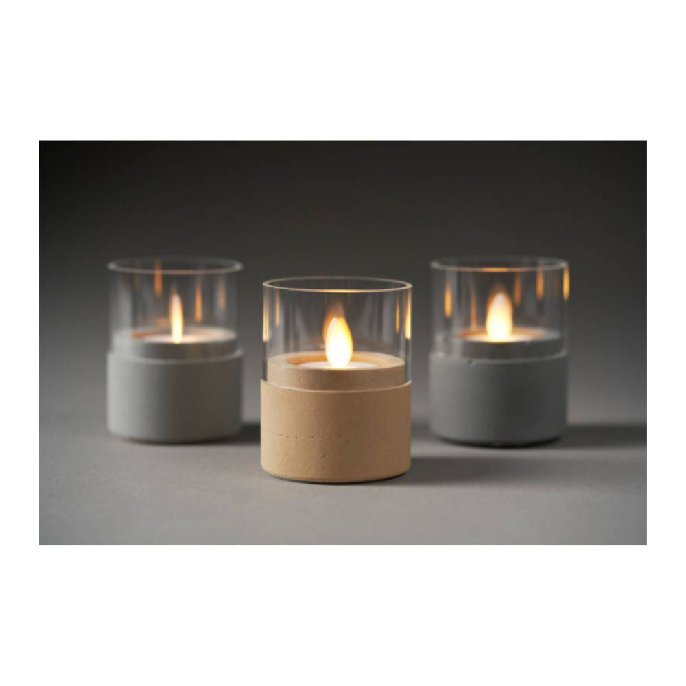 A LED Moving Flame candle (38x36 mm) from Duni GmbH with a realistic flickering effect sits on a gray surface in a glass holder with a concrete-like base, adding a modern touch with its warm light. Available in light and dark shades.