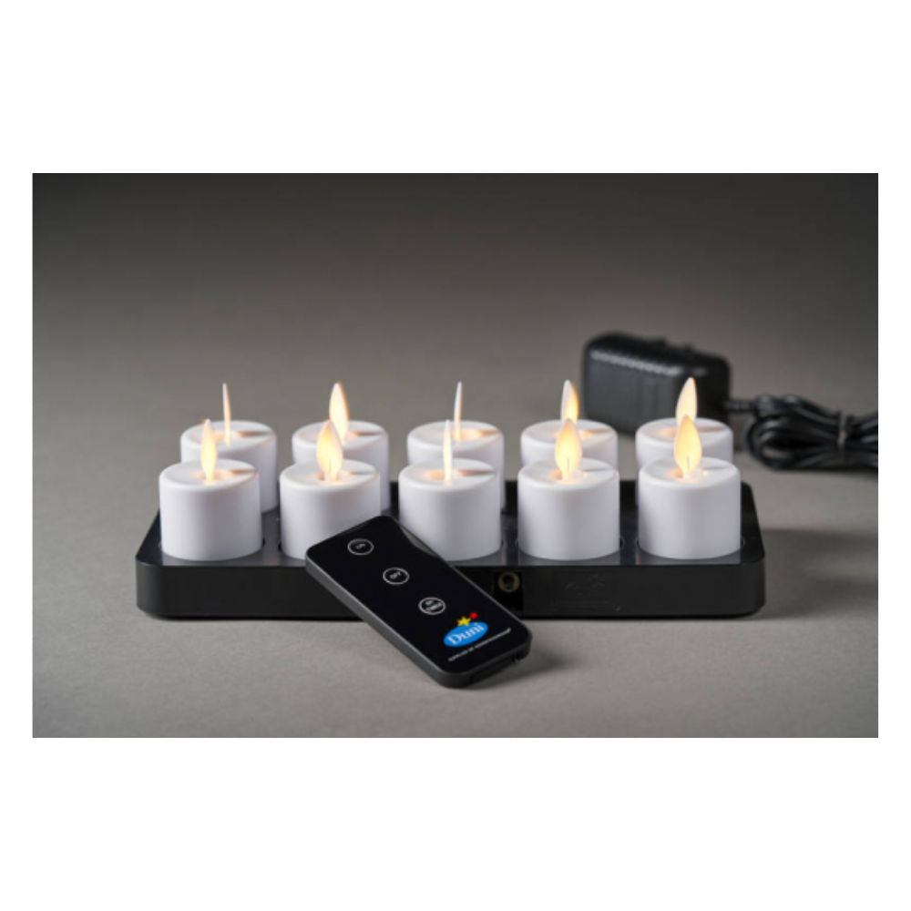 A Duni GmbH LED Moving Flame (38x36 mm, pack of 1 piece) with a realistic flickering effect is shown on a black charging station, with a matching remote control and power supply to the right.
