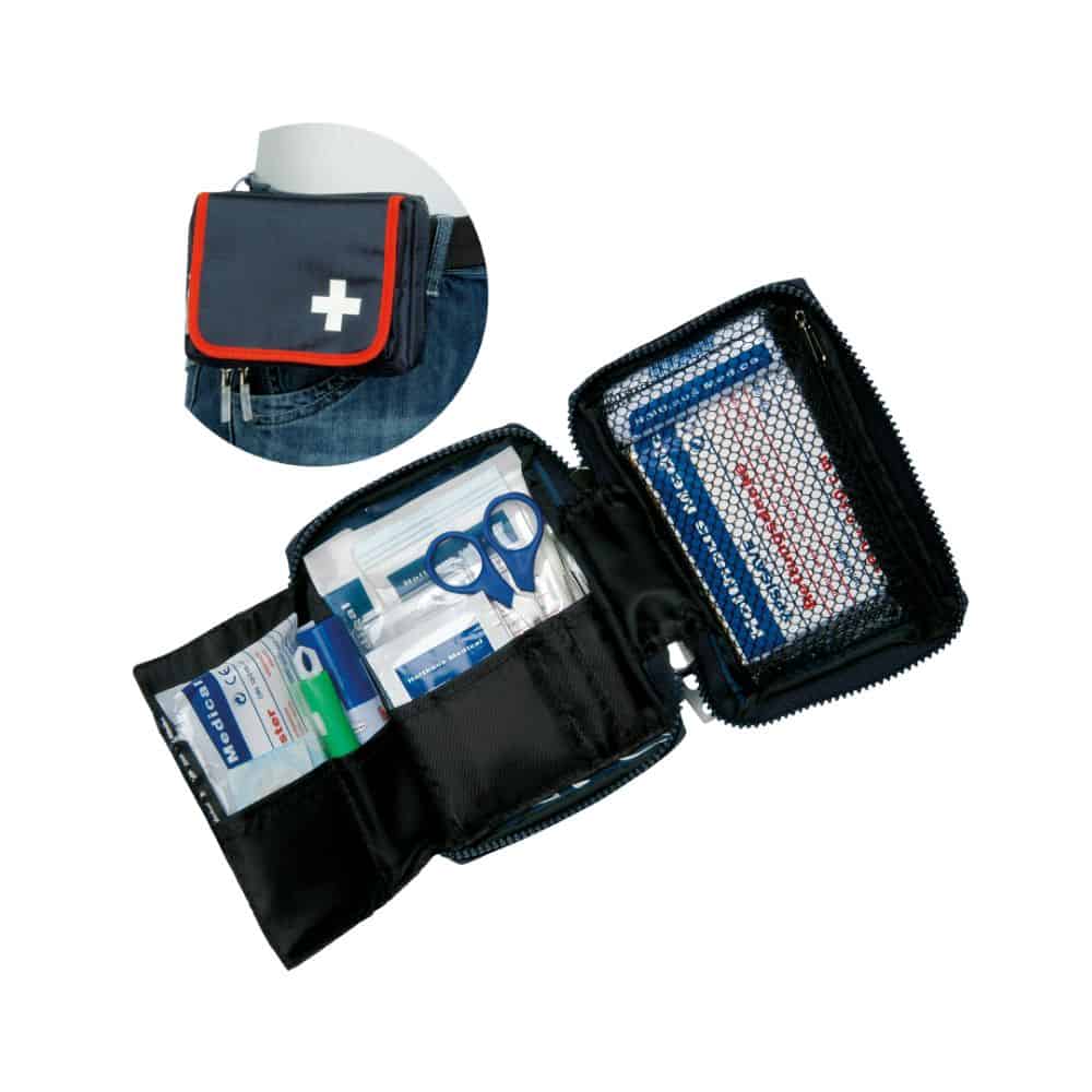 The Holthaus Medical first aid kit TRAVEL blue/red from Holthaus Medical GmbH & Co. KG is shown open and filled with medical supplies such as bandages, scissors, and antiseptic wipes. The cover is equipped with a white cross symbol and a belt attachment. An inserted image shows the set attached to a jeans belt.
