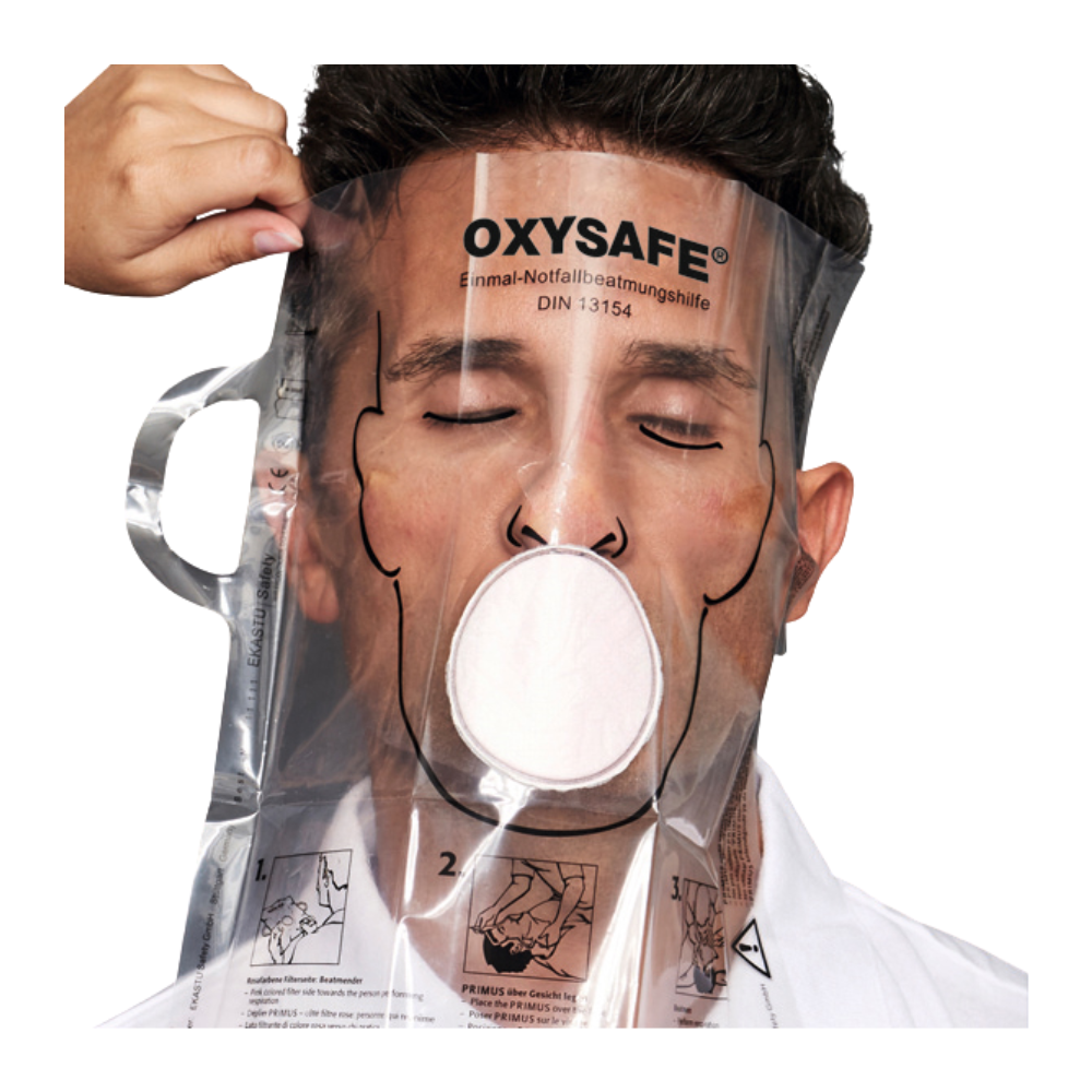 Eine Person trägt eine transparente Holthaus Oxysafe® Notfallbeatmungshilfe-Maske der Holthaus Medical GmbH & Co. KG und hat die Augen geschlossen, während eine andere Person die Maske anpasst. Das Produkt ist mit Anweisungen und Diagrammen versehen, die auf die Kunststoffoberfläche gedruckt sind.