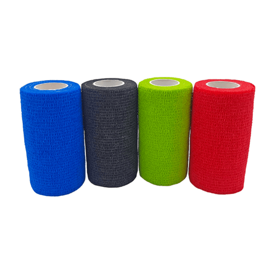 Four rolls of Holthaus VliVet® self-adhesive bandages for veterinary use, manufactured by Holthaus Medical GmbH & Co. KG, are lined up side by side. From left to right, the colors are blue, black, green, and red. The bandages have a textured surface and a cylindrical shape with a white inner core, making them ideal for hoof care in veterinary settings.