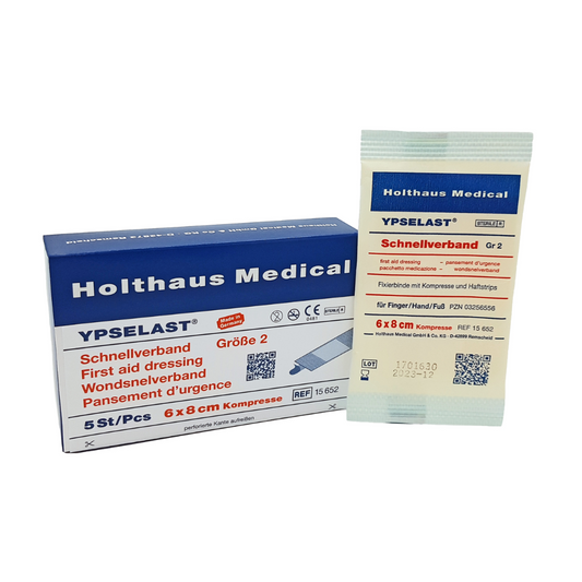 Auf dem Bild ist ein Holthaus Ypselast® Schnellverband der Holthaus Medical GmbH & Co. KG zu sehen. Links ist ein blau-weißer Karton mit der Aufschrift „Schnellverband Größe 2“ in den Maßen 6x8 cm zu sehen. Rechts ist eine der elastischen Fixierbinde in ihrer weißen Einzelverpackung abgebildet.