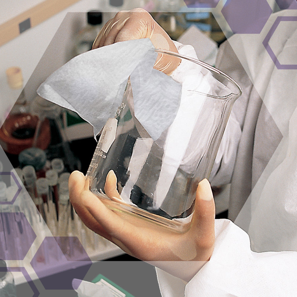 In einem Labor wischt eine Person mit Handschuhen und einem Laborkittel ein Klarglasbecherglas mit Kimtech® Pure Wischtücher - Viertelgefaltet / Weiß (12 Packs x 35 Blatt) aus dem 12-Päckchen Karton ab.