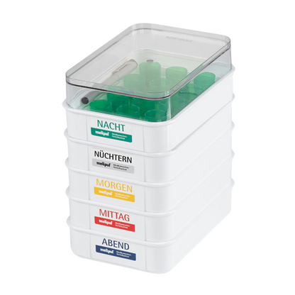 The SATZ melipul meal tray 12 with reusable cup, manufactured by Helmut Schwarz GmbH, consists of stacked plastic containers with German labels: "Night", "Fasting", "Morning", "Noon" and "Evening". These are ideal for medication administration in care facilities. Each container features transparent lids with green-sealed tubes and a visible marking in the top container.