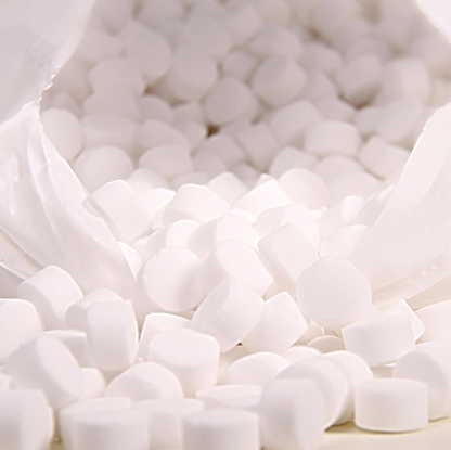 A close-up shows a white plastic bag with the inscription “K+S Minerals and Agriculture GmbH,” containing Regenit salt tablets according to EN 973 Type | Bag (25 kg) that fall onto a surface. The small, round tablets have a uniform shape and size and are ideal for use in water softening systems.