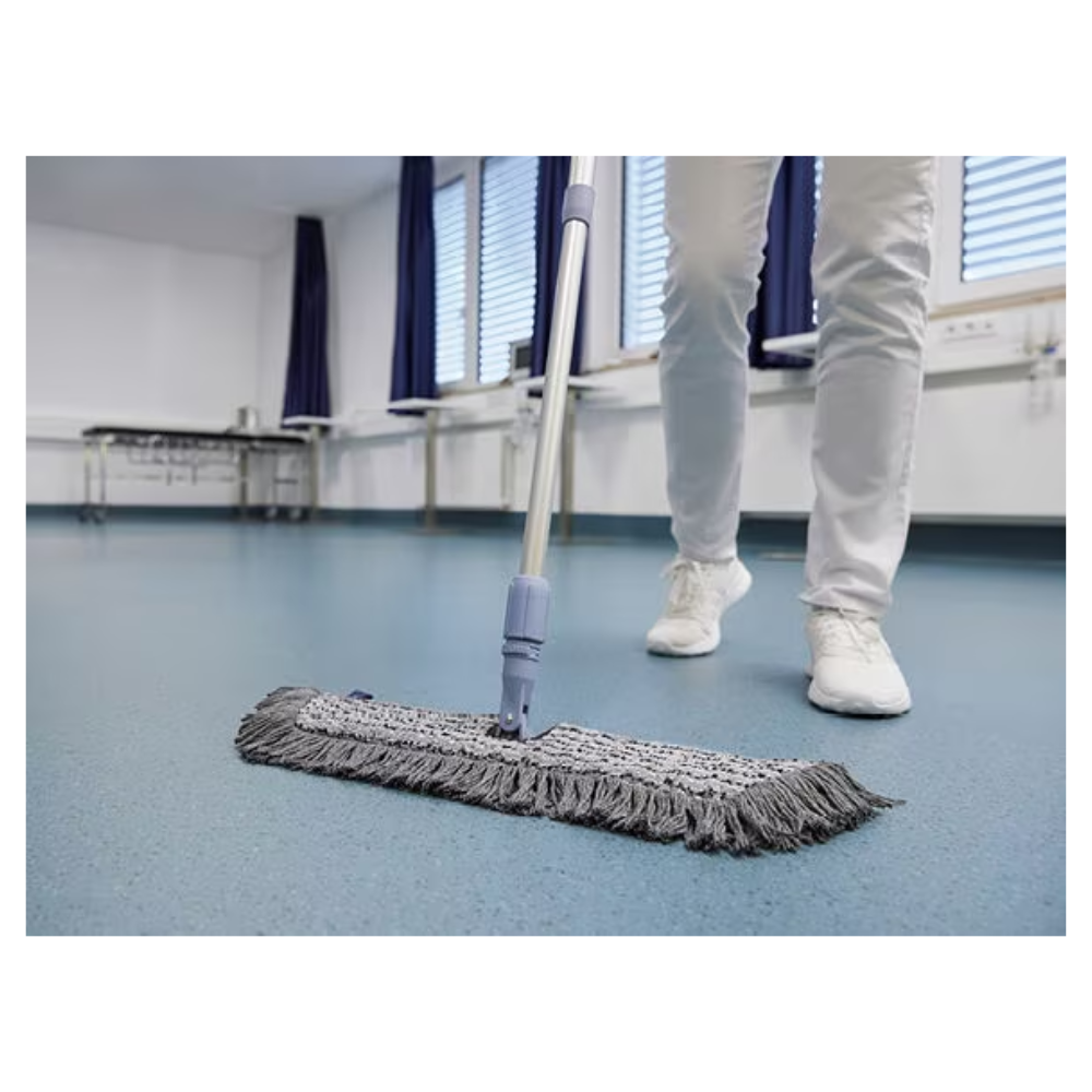 A person in white shoes and pants is mopping a blue floor with a Vileda GmbH Professional Swep Duo r-MicroCombi Mop - 50 cm in a room with closed blinds and blue curtains. A folding table stands nearby and a radiator is under the windows.