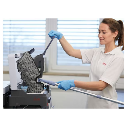 A person with blue gloves and a white shirt is cleaning a textured black surface with the Vileda Professional Swep Duo r-MicroCombi Mop - 50 cm from Vileda GmbH. The scene appears to be indoors, with a large window in the background through which natural light enters the room.