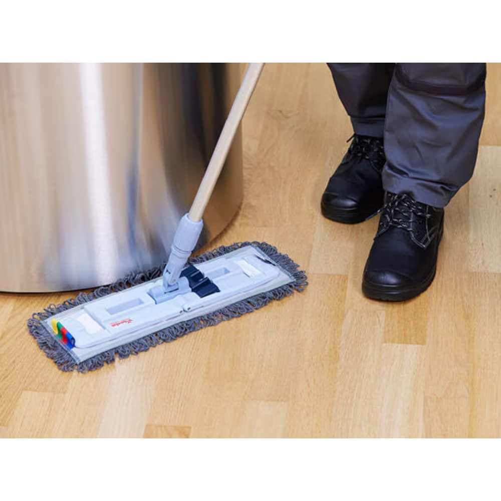 Eine Person in dunklen Schuhen und Hosen wischt einen hellen Holzboden mit einem Vileda Professional UltraSpeed Pro r-MicroSpeed Max Mop. Der Mop mit grauen Fransenkanten und verstellbarem Griff ist auf Effizienz ausgelegt. Im Hintergrund ist teilweise ein großes zylindrisches Metallobjekt zu sehen.