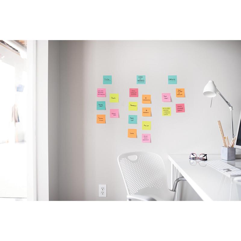 A white desk with a lamp, pen holder, and glasses stands next to a white chair. Above, in a bright office, Post-it® Super Sticky Notes (47.6 mm x 47.6 mm, 90 sheets/block, 100% PEFC) from 3M Deutschland GmbH are attached to the wall.