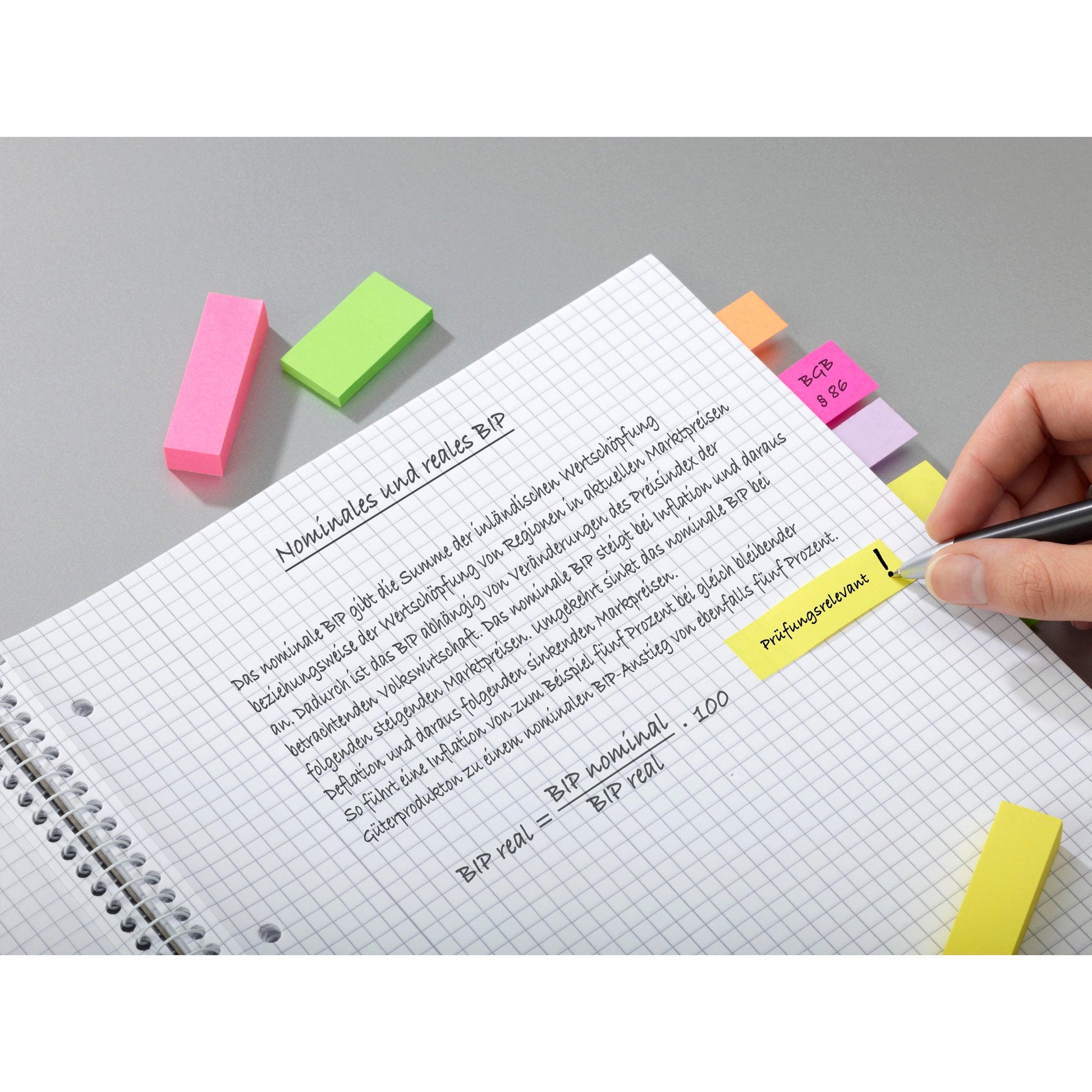 Eine Hand schreibt auf einem karierten Notizbuch mit hervorgehobenen deutschen Notizen über "nominales und reales BIP". In der Nähe befinden sich Post-it® Page Marker, Energetic Collection (25x76 mm, 3er-Pack) der 3M Deutschland GmbH. Bunte Klebelaschen ordnen die Seite.