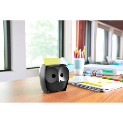 A Post-it® Z-Notes Dispenser, Owl, Black from 3M Deutschland GmbH stands on a wooden table with notebooks, a cup, colored pencils in a cup, and Post-it® Super Sticky Z-Notes (45 sheets/block, 2 blocks/pack); large windows offer a view of trees.