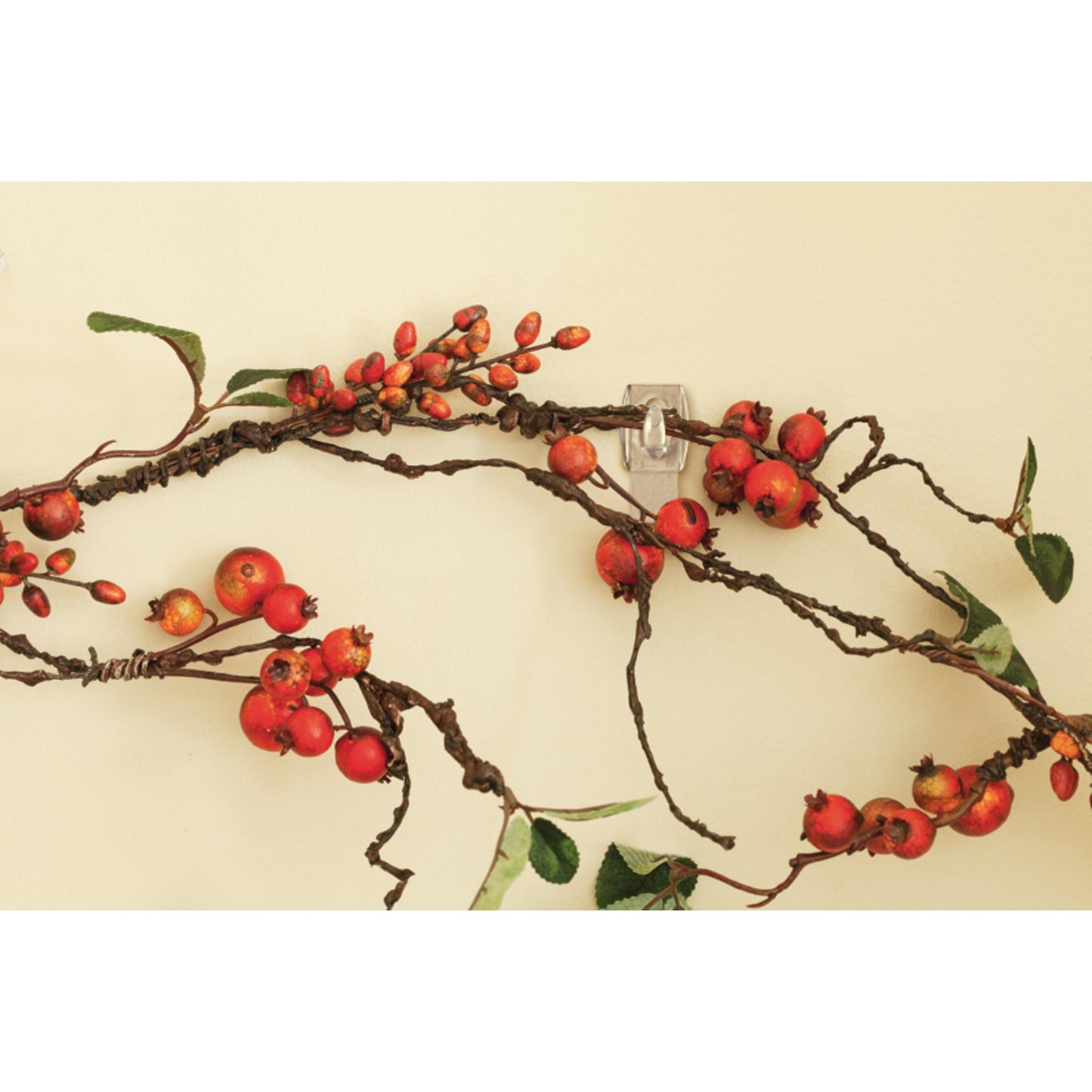 Ein dekorativer Zweig mit roten Beeren und grünen Blättern hängt an einer hellen Wand, spurlos befestigt mit dem Command™ Mini-Haken, transparent, mit transparenten Strips (17006CLR) von 3M Deutschland GmbH.