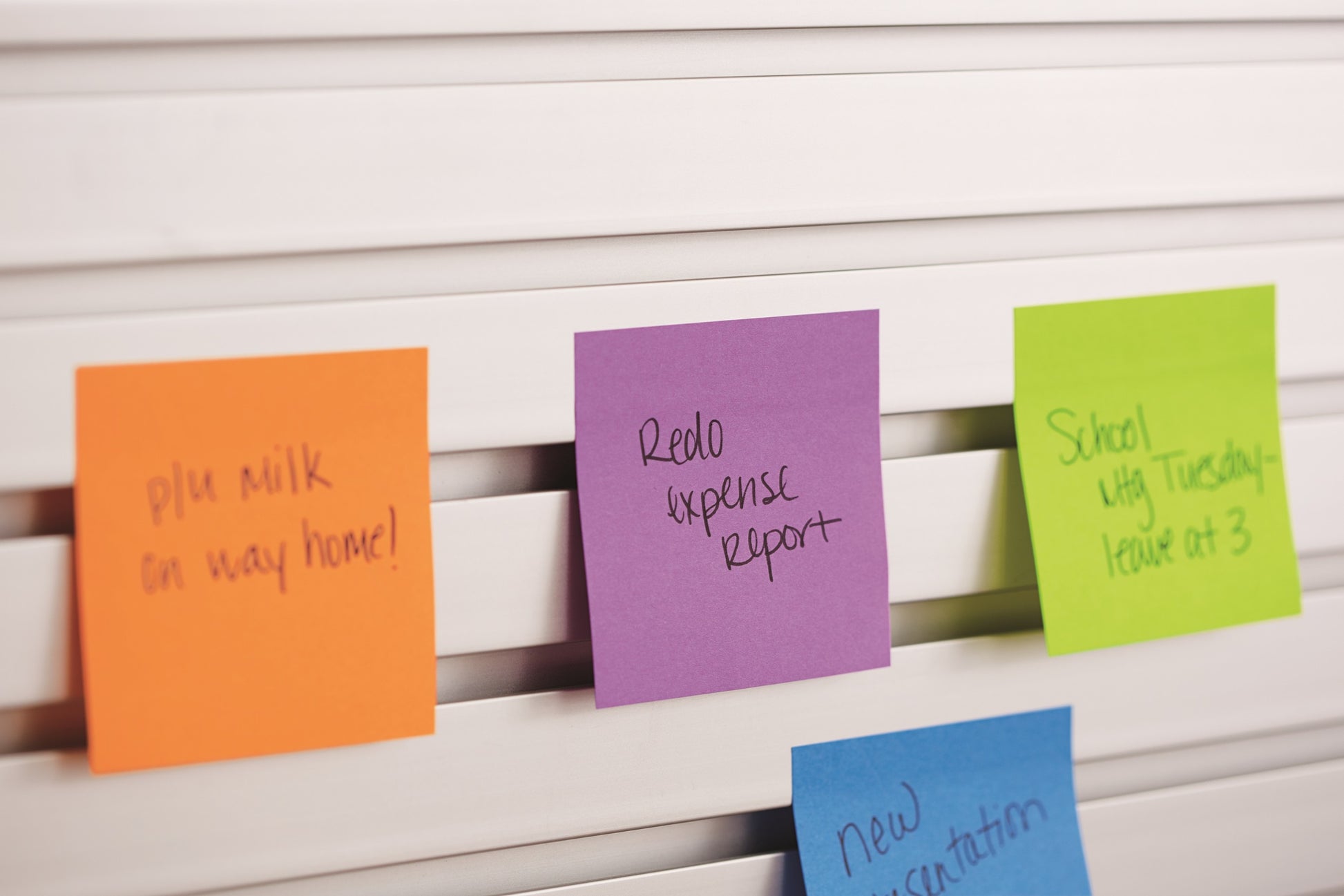 Drei 3M Post-it® Notes in verschiedenen Neonfarben (38mm x 51mm, 100 Blatt/Block, 3 Blöcke/Packung) sind an einer weißen Lamellenfläche angebracht und zeigen Erinnerungen und Notizen.