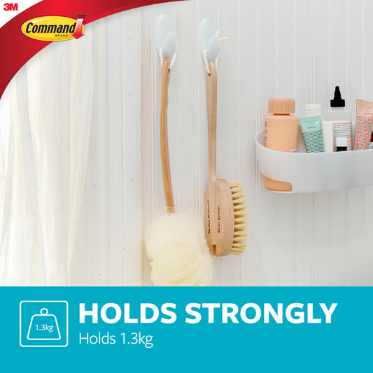 Ein Badezimmer mit zwei Command™ Bad Handtuchhaken von 3M Deutschland GmbH, die hölzerne Badebürsten neben einem Duschvorhang halten; ein weißes Wandregal enthält Toilettenartikel. Text: "Holds Strongly. Hält 1,3 kg." Command- und 3M-Logos sichtbar.