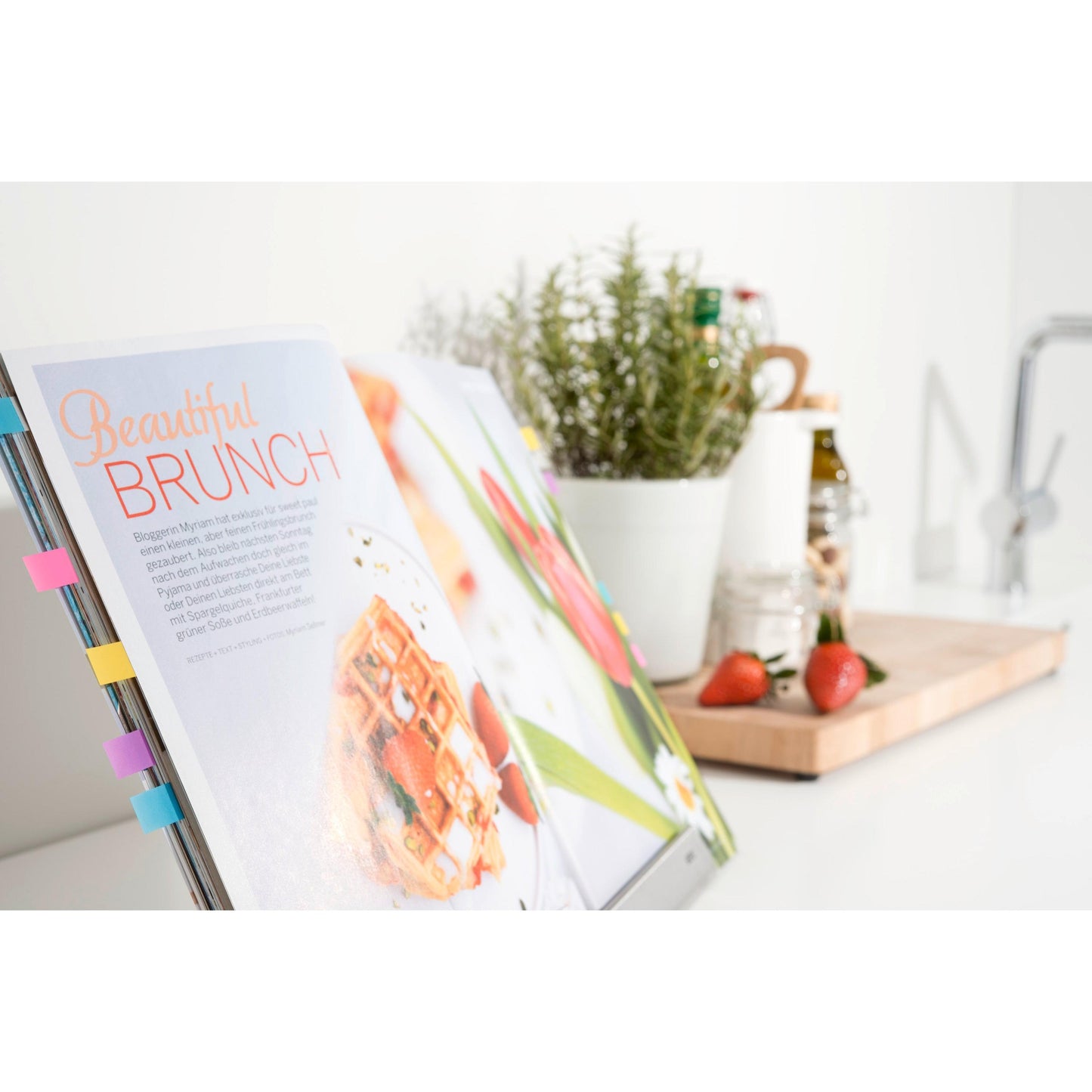 On a kitchen table, an open cookbook is marked with colorful Post-it® Index Mini Tabs (11.9 mm x 43.2 mm, 4+2 free per pack, 3M Deutschland GmbH). Nearby, a pot with herbs and strawberries stands against a white background.