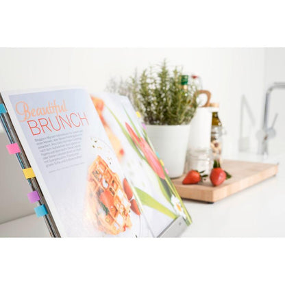 A cookbook labeled with Post-it® Index Tabs Mini (11.9 x 43.2 mm, 100/dispenser) from 3M Deutschland GmbH features a brunch recipe; behind it are a white herb pot, strawberries on a board, and kitchen utensils on a sunlit counter.