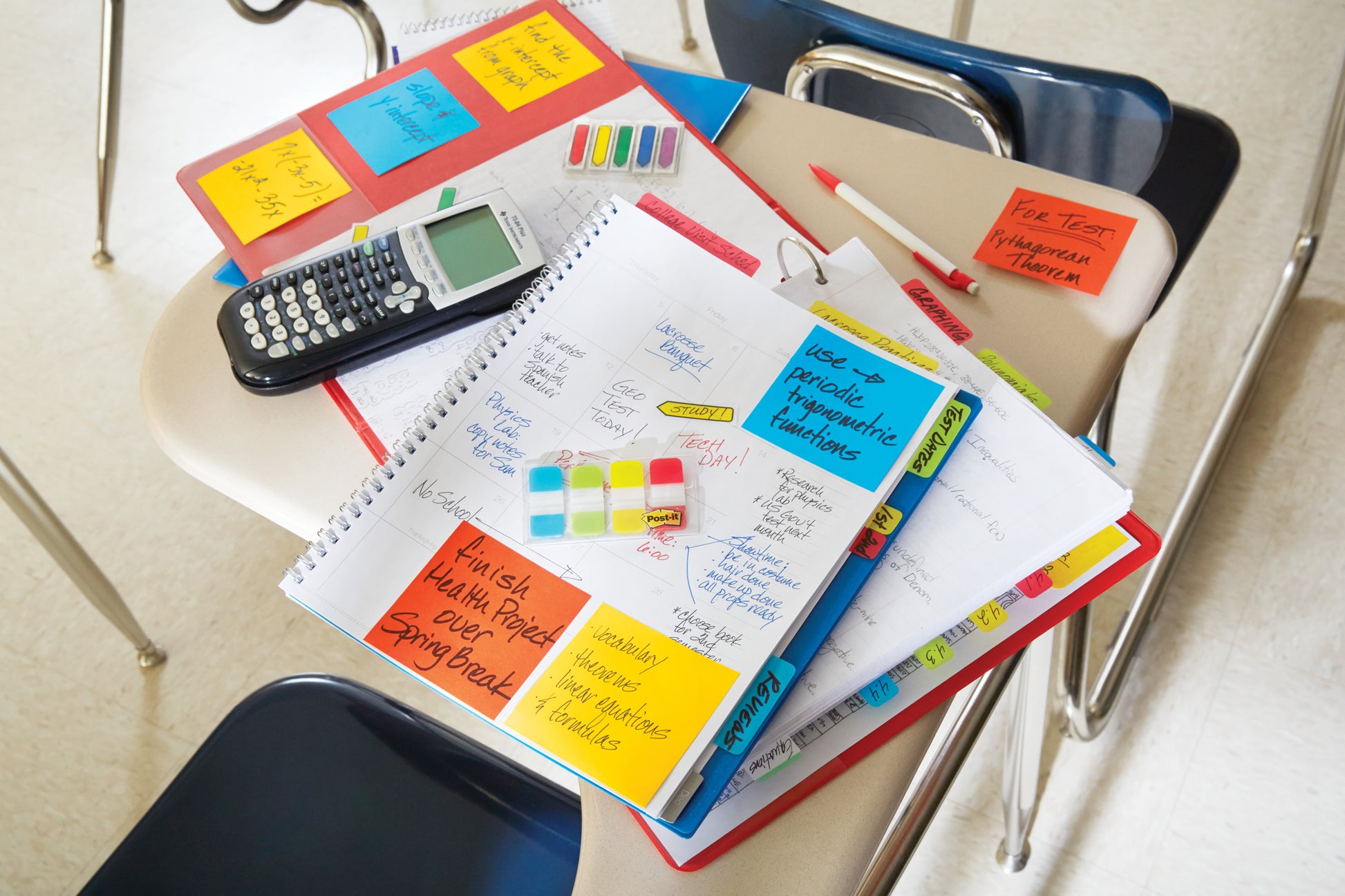 Auf einem Schülerschreibtisch befinden sich Hefte, Papiere, ein Taschenrechner und bunte Stifte, die mit dem Post-it® Z-Notes Dispenser PRO (Schwarz) und Super Sticky Z-Notes (Gelb), 76x76mm, von 3M Deutschland GmbH für handschriftliche Mathe-Erinnerungen organisiert sind.
