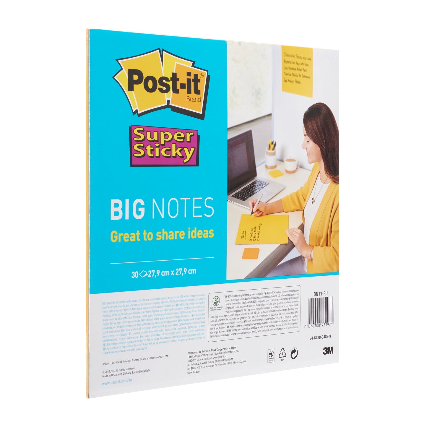 A person writes at a desk on a 3M Deutschland GmbH Post-it® Super Sticky Big Notes BN11-EU pad (279x279mm, yellow, 30 sheets, 100% PEFC). The packaging with branding and info is seen next to a laptop and a notebook.