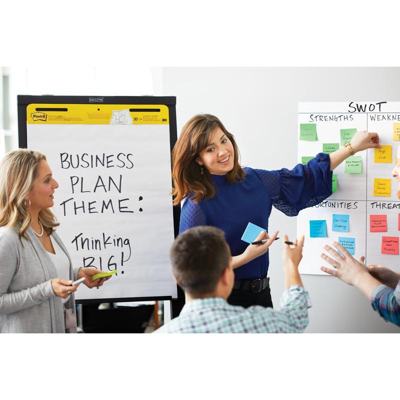 In a meeting room, a woman points to a SWOT diagram covered with pink Post-it® Super Sticky Z-Notes (76x76mm) from 3M Deutschland GmbH, while another stands next to a flipchart; nearby is a white Post-it® Z-Notes Dispenser "Cat".