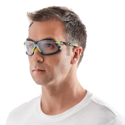 A man with short brown hair wears the 3M™ Solus™ Safety Glasses 1000 with green and black accents and clear lenses from 3M Deutschland GmbH, slightly turned to the side in a plain white T-shirt against a white background.